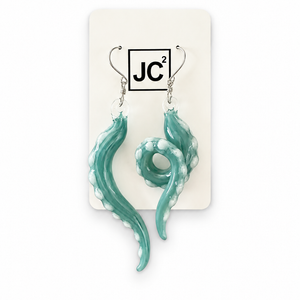 Asymmetrical silveraqua glass tentacle earrings with white suckers, one long and one curled, on silver hooks displayed on a white JC2 card.