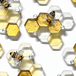 Beecline glass wall sculpture with clear and golden hexagonal honeycomb cells, flameworked glass bees, and round silver mounting hardware.
