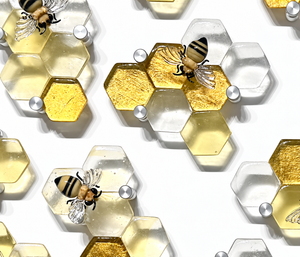 Beecline glass wall sculpture with clear and golden hexagonal honeycomb cells, flameworked glass bees, and round silver mounting hardware.
