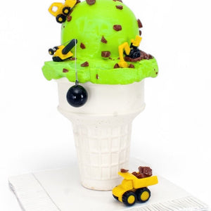 Chocolate Party glass sculpture with a bright green ice cream scoop, brown chocolate pieces, and miniature yellow construction vehicles atop a white cone