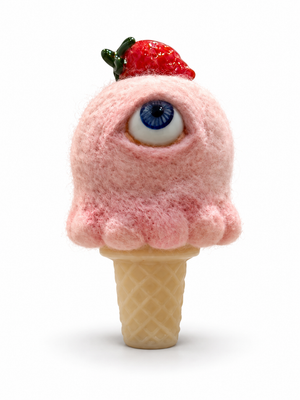 Pink needle-felted wool ice cream sculpture with a single blue eye, a glass strawberry on top, and a yellow cast glass cone.
