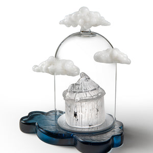 Look Out...side glass sculpture featuring a small white round building beneath a clear dome, surrounded by white clouds on a blue cloud-shaped base.

