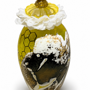 Sweetness glass sculpture with a bee perched on a yellow flower above white blossoms and a rounded vessel with honeycomb imagery and mottled brown-and-white details.