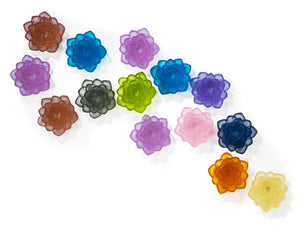 Wall Installation of cast glass water lilies with layered petals in blue, purple, pink, gray, lime green, orange, and yellow on a white background.
