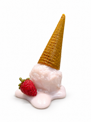 Glass sculpture of an upside-down golden waffle cone on a pale pink scoop melting into a puddle, with a red glass strawberry beside it on a white background